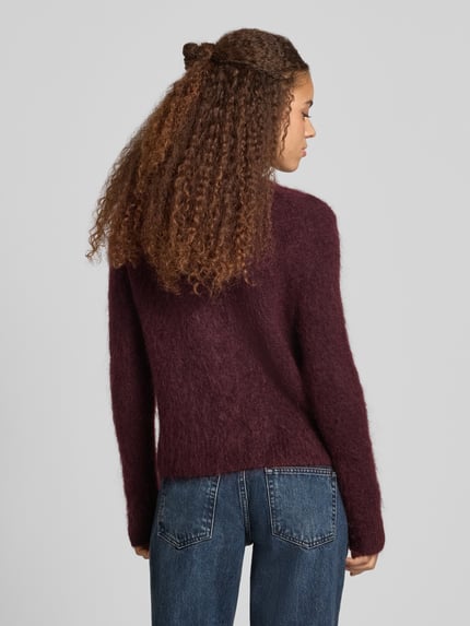 Frauenmodel trägt Cardigan aus Mohair mit Label-Schriftzug von Marc O'Polo in unifarbener, strukturierter Strickoptik, Ganzkörperansicht Rückansicht.