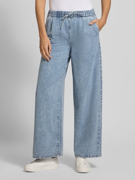 Männermodel trägt Wide Leg Jeans aus bawełny i wiskozy Modell 'VALERIA' von Vero Moda, stylizowana na denim, krój wide fit, tunel, elastyczny ściągacz, wpuszczane kieszenie, imitacja kieszeni z tyłu; jasnoniebieski, gładka faktura, Ganzkörperansicht von vorne.
