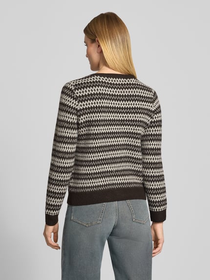 Frauenmodel trägt Cardigan mit Zierknöpfen von VERO MODA in Strickoptik mit geometrischem Allover-Muster, Erdtöne, Ganzkörperansicht Rückansicht.