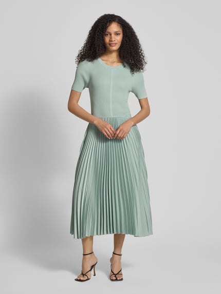 Modelka prezentuje Regular Fit Businesskleid aus verschiedenen Materialien Modell 'FADRIDI' von BOSS, efekt: jednolity kolor, długość midi, okrągły dekolt, spódnica plisowana z satyny, krótki rękaw, wykończenie materiału: prążkowana dzianina i satyna, plisowana tekstura, Ganzkörperansicht von vorne.