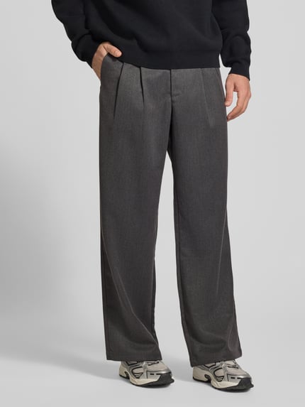 Mężczyzna nosi spodnie z zakładkami w pasie Bundfaltenhose mit Gesäßtaschen Modell 'HERITAGE' od PROHIBITED, Mieszanka materiałów z dodatkiem wiskozy, krój regular fit, kieszenie z tyłu, szerokość w rozmiarze M: 46 cm, długość wewnętrzna nogawki w rozmiarze M: 80 cm, szare odcienie, gładka tekstura, klasyczny fason, Ganzkörperansicht von vorne.