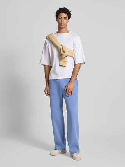 Männermodel trägt Loose Fit Sweatpants mit Seitentaschen van REVIEW in lichtblauw katoenmix met labelprint, elastische band, zijzakken, achterzak, binnenbeenlengte maat M 80 cm, ganzkörperansicht von vorne.