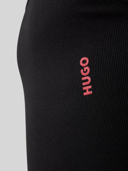 Männermodel trägt Tanktop mit Label-Print im 2er-Pack von HUGO aus schwarzem Baumwoll-Elasthan-Mix in Ripp-Optik, Detailaufnahme.