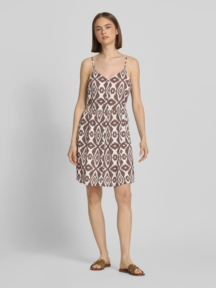 Frauenmodel trägt Leicht ausgestelltes Minikleid aus reiner Viskose Modell 'TALA' von Pieces mit floralem Allover-Muster, Mini-Länge, V-Ausschnitt, verstellbaren Spaghettiträgern in hellbraun und weiß, Ganzkörperansicht von vorne.