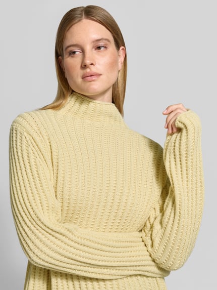 Frauenmodel trägt Strickpullover mit Stehkragen Modell 'ARWIE' von DRYKORN, hellgelb, grobe Rippenstruktur, Regular Fit, Nahaufnahme Oberkörper, Materialmix mit Alpaka-Anteil.