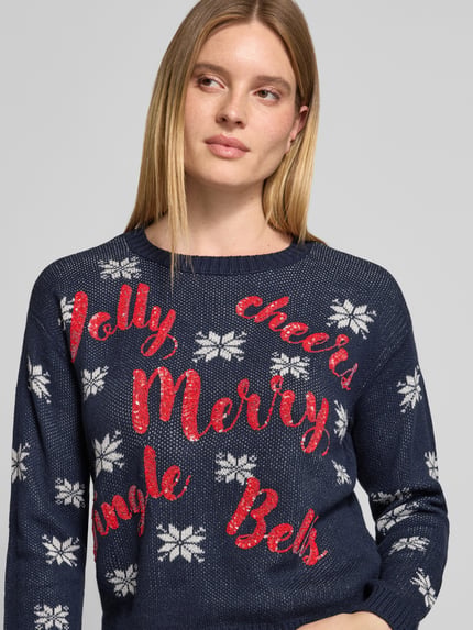 Frauenmodel trägt Pullover mit Pailletten-Schriftzug von VERO MODA in mehrfarbiger Strickoptik mit Sternenmuster, Nahaufnahme Oberkörper.