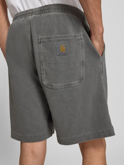 Männermodel trägt Regular Fit Shorts mit elastischem Bund Modell 'Harper' von Carhartt Work In Progress aus Reine gewachste Baumwolle, dezentes Grau, strukturierte Oberfläche, Herren Shorts, Ganzkörperansicht Rückansicht.