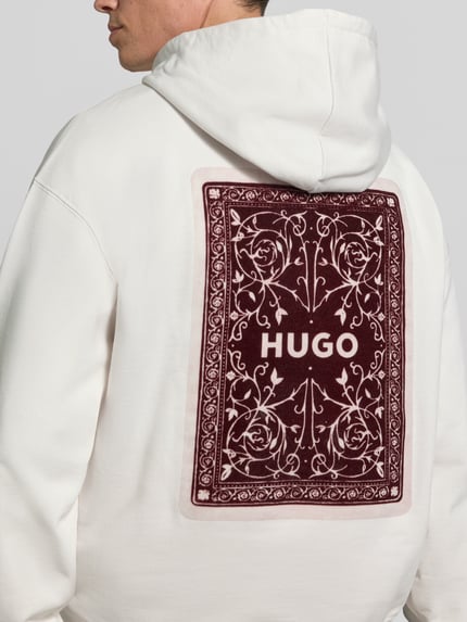 Männermodel trägt Hoodie mit großem Rückenprint Modell 'Dewerhood' von HUGO in Weiß mit bordeauxfarbenem Motiv-Print, Jersey, Ganzkörperansicht Rückansicht.