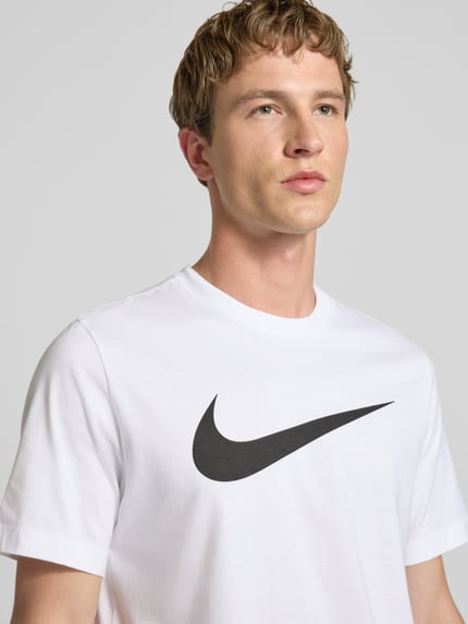Męski model nosi t-shirt z bawełny prosty krój, model 'Swoosh' z okrągłym dekoltem, nadruk z logo; t-shirt z logo-Print model 'Swoosh' od Nike, długość tyłu w rozmiarze M: 73 cm; zbliżenie górnej części ciała.