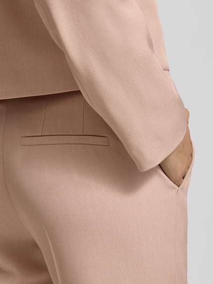 Frauenmodel trägt Stoffhose mit Gesäßtasche von Jake*s Collection in Beige, leichte Struktur, Material-Mix, Detailaufnahme Hüfte und Gesäß.