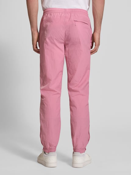 Männermodel trägt Straight Fit Stoffhose mit Logo-Stitching Modell 'Nayla' von SERGIO TACCHINI in Rosa, elastischer Bund mit Tunnelzug, elastische Beinabschlüsse, Innenbeinlänge bei Größe M 77 cm, Ganzkörperansicht Rückansicht.