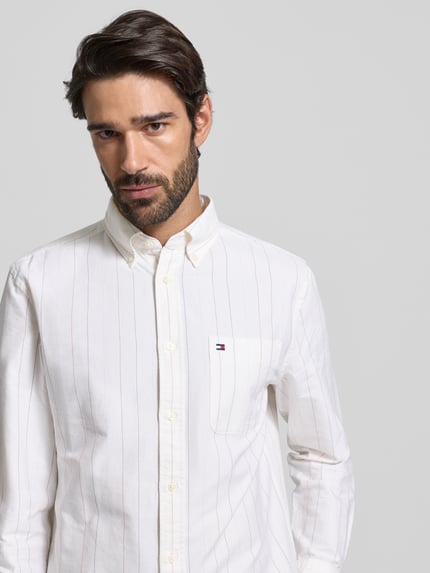 Männermodel draagt Regular Fit Vrijetijdsoverhemd uit puur katoen van Tommy Hilfiger, gestreept, effen kleuren, logodetail, knoopsluiting, borstzak, button-downkraag, lange mouw, afgeronde rompzoom, sportmanchet, rugpas met plooi, motiefdetails, materiaal puur katoen. Nahaufnahme Oberkörper.