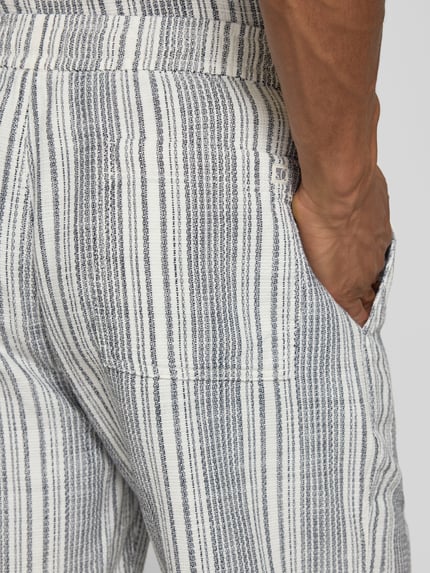 Mężczyzna nosi Relaxed Fit Shorts aus reiner Baumwolle od s.Oliver RED LABEL, efekt: w paski, wykończenie: bouclé, bawełna, wpuszczane kieszenie, tunel, elastyczny ściągacz, zapięcie: tunel, detal: logo, ujęcie: z tyłu, zbliżenie na kieszeń.
