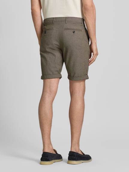 Mężczyzna model nosi Slim Fit Chinoshorts aus Baumwoll-Mix Modell 'LUTON' von SELECTED HOMME, brązowy, drobna faktura, jednokolorowe, krój slim fit, szlufki na pasek, zapięcie na guzik i ukryty zamek, boczne kieszenie, tylne kieszenie z guzikiem, bawełniany miks, widok całej sylwetki z tyłu.