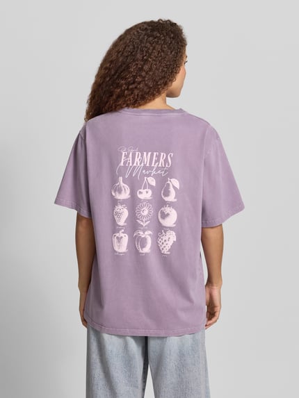 Frauenmodel trägt Damen T-Shirt von OH APRIL in Flieder mit Oversized-Schnitt, Rundhalsausschnitt, Label-Stitching, Reine Baumwolle, Rückansicht, Rückenlänge bei Größe S: 72 cm, Modell 'Farmers Market'.