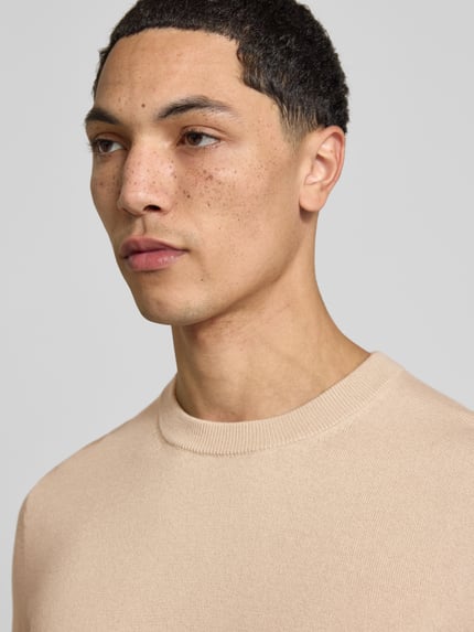 Männermodel trägt Wollpullover mit gerippten Abschlüssen von Filippa K, Rundhalsausschnitt, beige Farbe, Nahaufnahme Oberkörper. Woll-Baumwoll-Mix, gerader Schnitt, Rückenlänge bei Größe M 68 cm.