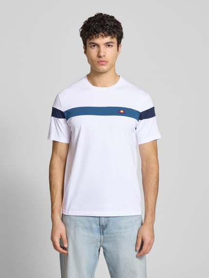 Männermodel trägt Regular Fit T-Shirt mit Logo-Detail Modell 'Caserio' von Ellesse aus reiner Baumwolle, weiß mit blauen Streifen, Kurzärmelig, Rundhalsausschnitt, Rückenlänge bei Größe M 68 cm, Ganzkörperansicht von vorne.