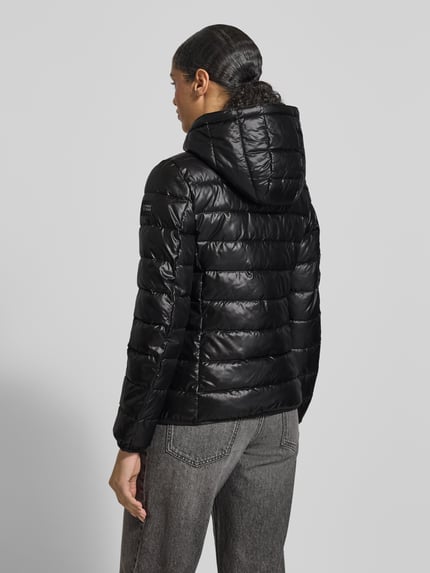 Frauenmodel trägt schwarze Jacke mit Kapuze von NAUTGÅRD, lockerer Schnitt, Label-Detail, Rückenansicht, Ganzkörperansicht Rückansicht.