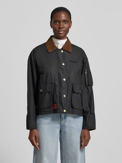 Vrouwenmodel draagt Jacke aus Baumwolle mit Pattentaschen van Original Bombers, zwart, puur katoen, regular fit, platte kraag, knoopsluiting, klepzakken, ruglengte maat S 60 cm, schouderbreedte 52 cm, borstwijdte 58 cm, mouwlengte 57 cm, voorkant volledige lichaamsopname.