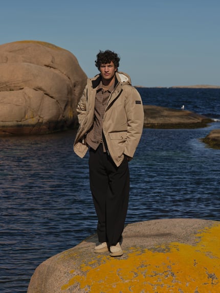 Männermodel trägt Stoffhose mit Bügelfalte Modell 'LEEK' von DRYKORN, weiter Schnitt, Schwarz, glatte Textur, Ganzkörperansicht von vorne.