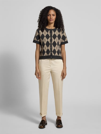 Modelka nosi Slim Fit Chino aus Baumwoll-Satin od s.Oliver BLACK LABEL, jasny beż, satynowy bawełniany materiał, krój slim fit, kanty, elastyczny pas, kieszenie boczne oraz imitacja kieszeni z tyłu, długość do kostek z mankietem; widok całej sylwetki z przodu.
