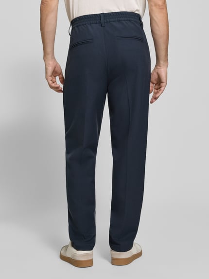 Männermodel trägt dunkelblaue Hose mit elastischem Bund und Bügelfalten Modell 'MARC 2.0' von Casual Friday, Ganzkörperansicht Rückansicht, Material-Mix mit Viskose-Anteil, Regular Fit, Eingrifftaschen, Paspeltaschen am Gesäß.