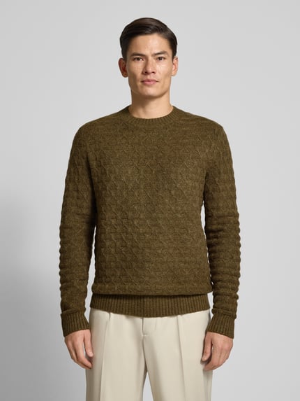 Męski model nosi Strickpullover mit gerippten Abschlüssen Modell 'BLASIMON' od Jack & Jones Premium, oliwkowy sweter z okrągłym dekoltem i prążkowanymi brzegami, regular fit, mieszanka z wełną, widok całej sylwetki z przodu.
