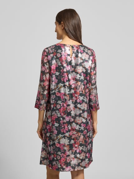 Vrouwenmodel draagt 'Knielanges Kleid mit Allover-Muster und Paillettenbesatz' van Christian Berg Woman in roze, zwart en wit met bloemenpatroon, rechte snit, ronde hals, 3/4 mouw, detail op de rug, pure viscose, knielengte, totale ruglengte 96 cm bij maat 36, borstwijdte 48 cm bij maat 36, mouwlengte 47 cm bij maat 36. Volledig lichaam achteraanzicht.