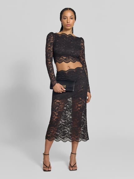 Frauenmodel trägt Cropped Langarmbluse aus Spitze von Rabanne in Schwarz, eng anliegend, semitransparent, Ganzkörperansicht von vorne.