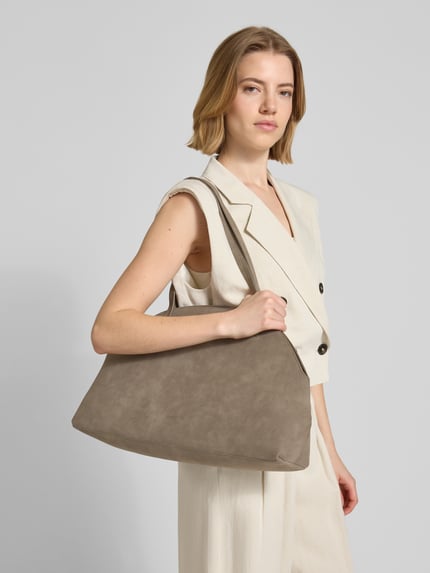 Frauenmodel trägt Handtasche mit Logo-Prägung Modell 'Balour' von Someday in Taupe, glatte Struktur, smarte Schulterriemen, Ganzkörperansicht von vorne.