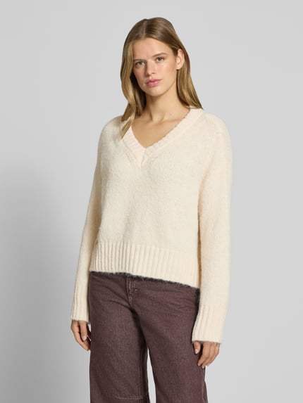Frauenmodel trägt Pullover mit tiefem V-Ausschnitt von ONLY in Creme, lockere Form, weiche Struktur, Ganzkörperansicht von vorne. Damen Pullover von ONLY.