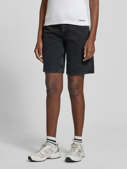 Frauenmodel trägt Regular Fit Jeansshorts aus reiner Baumwolle Modell 'THALINAA' von Armedangels in schwarzer Denim-Optik, 5-Pocket-Design, Ganzkörperansicht von vorne.