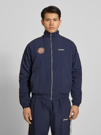 Männermodel trägt dunkelblaues Trackjacket mit Label-Stitching Modell 'Slipstream' von PROHIBITED, Relaxed Fit, Stehkragen, Reißverschluss, Ganzkörperansicht von vorne.