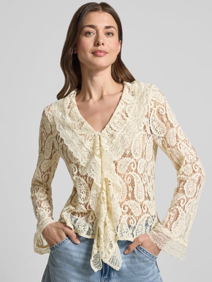 Frauenmodel trägt Regular Fit Regular Fit aus Baumwoll-Mix Modell 'SALLY' von Vero Moda, semitransparente Langarmbluse mit abstraktem Muster, Rüschenkragen und tiefer V-Ausschnitt, cremefarbene Spitze mit floraler Textur, Nahaufnahme Oberkörper.