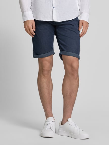 Männermodel trägt Jeansshorts mit Label-Detail von Pierre Cardin in Dunkelblau, Baumwoll-Mix mit Stretch-Anteil, Eingrifftaschen, Umschlag, Regular-Fit, Ganzkörperansicht von vorne.