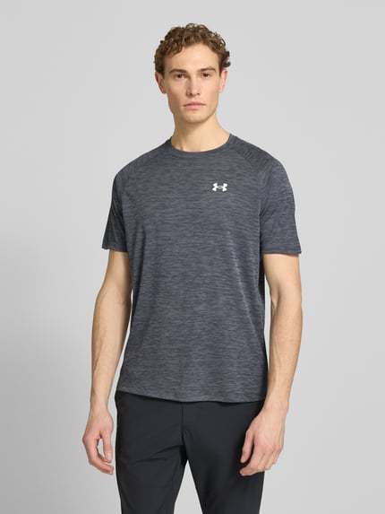 Männermodel trägt Herren T-Shirt mit Label-Print Modell 'Tech' von Under Armour, Grautöne, strukturierte Optik, Gerader-Schnitt, Rundhalsausschnitt, Rückenlänge bei Größe M 75 cm, Ganzkörperansicht von vorne.