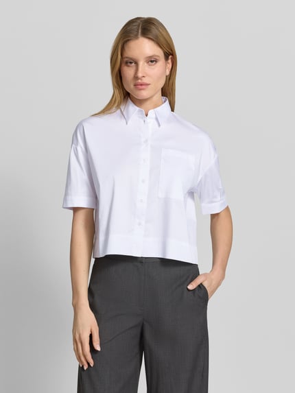 Frauenmodel trägt Hemdbluse mit Brusttasche und Kentkragen von More & More aus weißem Baumwoll-Mix mit Stretch-Anteil, Regular-Fit, Knopfleiste, leicht überschnittene Schultern, Rückenlänge 53 cm, Ärmellänge 30 cm, Ganzkörperansicht von vorne.