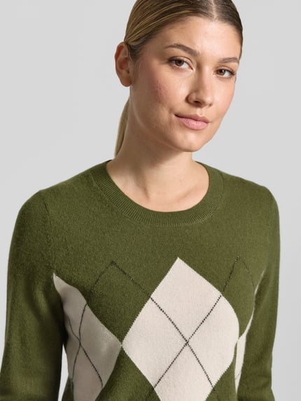Modelka kobieca nosi Slim Fit Strickpullover aus Kaschmir-Mix mit Rundhalsausschnitt od Christian Berg Woman, wzór w romby, zielony i kremowy, faktura dzianiny, krój slim fit, długie rękawy, długość tyłu w rozm. S: 54 cm, długość rękawa w rozm. S: 63 cm, widok na górną część ciała z przodu.