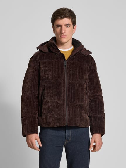 Männermodel trägt Pufferjacke mit abnehmbarer Kapuze von BOSS Orange in brauner Struktur-Optik aus Cord, Reißverschlusstaschen, Ganzkörperansicht von vorne
