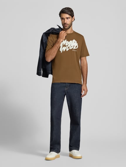 Männermodel trägt T-Shirt mit Label-Print Modell 'Bobby' von Wood Wood in Braun, Regular Fit aus Baumwolle, Ganzkörperansicht von vorne.