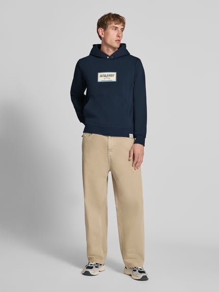 Männermodel trägt Hoodie mit Label-Print Modell 'FREDERIKSBERG' von JACK & JONES in Dunkelblau, lockerem Schnitt, Ganzkörperansicht von vorne, Baumwoll-Mix, Kängurutasche, gerippte Abschlüsse.