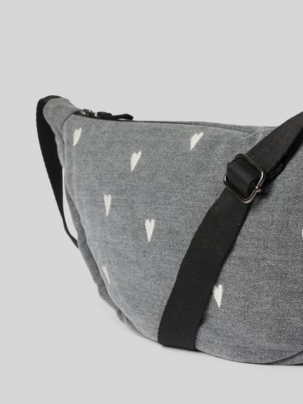Produktfoto, Fanny Pack aus reiner Baumwolle in Denim-Optik von Studio Noos z wyhaftowanym motywem na całej powierzchni, detal z logo, główna przegroda z zamkiem błyskawicznym, regulowany pasek na ramię, szerokość w rozmiarze 1: 40 cm, długość w rozmiarze 1: 21 cm, głębokość w rozmiarze 1: 11 cm, długość paska na ramię w rozmiarze 1: 118 cm