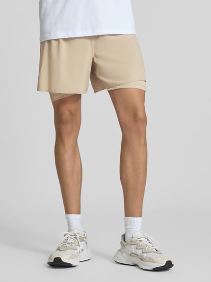 Männermodel trägt Regular Fit Sportshorts mit Logo-Print Modell 'ADI365/// 2i1 M' von adidas, beige Farbe, adidas Training, Nahaufnahme Unterkörper.