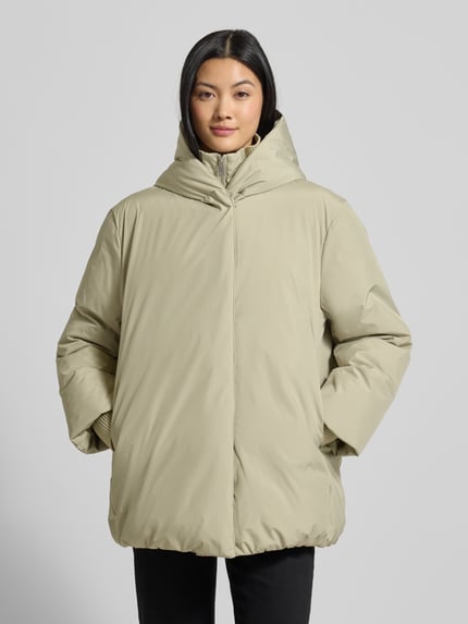 Frauenmodel trägt Regular Fit Outdoor-Jacke mit Stehkragen Modell 'Helah' von OPUS in Beige, glatte Oberfläche, elastische Ärmelabschlüsse, Ganzkörperansicht von vorne. Rückenlänge 74 cm, Schulterbreite 53 cm, Brustweite 54 cm, Ärmellänge 63 cm, Kapuze integriert.