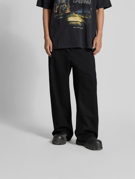 Männermodel trägt Straight Fit Hose aus Schurwoll-Mix von VETEMENTS, schwarze Farbe, Bundfalten, Gesäßtaschen, Nahaufnahme Unterkörper, Ganzkörperansicht von vorne.