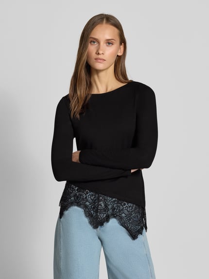Modelka nosi czarną bluzkę z długim rękawem z mieszanki wiskozy ze zdobionym koronką dołem, Slim Fit Langarmshirt aus Viskose-Mix Modell 'LAILA' von ONLY, damska bluzka z długim rękawem od ONLY, zdjęcie całej sylwetki z przodu.