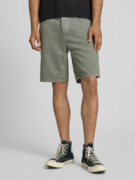 Männermodel trägt Regular Fit Jeansshorts aus reiner Baumwolle Modell 'EDGE' von Only & Sons in grüner Denim-Optik mit Nieten, Label-Patch, 5-Pocket-Design und Knopf mit verdecktem Reißverschluss, Material reine Baumwolle, Nahaufnahme Oberschenkel.