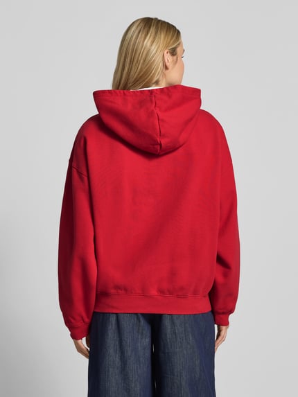 Vrouwenmodel draagt Oversized Hoodie uit puur katoen van Anine Bing in rood met kangoeroezak en ribboorden, ruglengte maat S 65 cm, geheellichaamsaanzicht rugzijde.