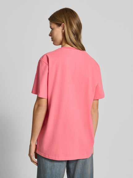Frauenmodel trägt T-Shirt mit Statement-Print und Rundhalsausschnitt von OH APRIL in Pink, Oversized, Reine Baumwolle, Rückenlänge 70 cm, Ganzkörperansicht Rückansicht.
