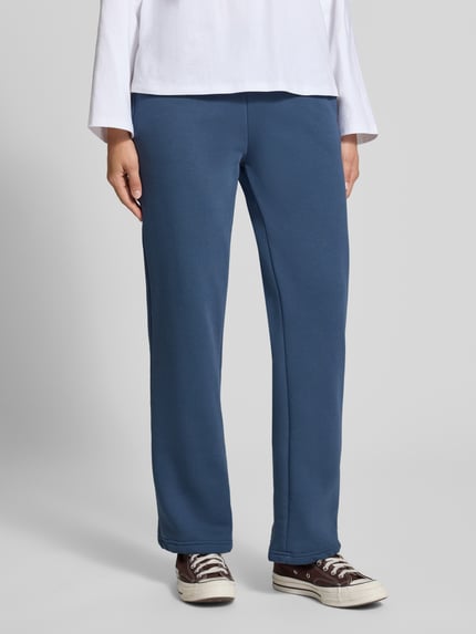 Frauenmodel trägt Sweatpants aus Baumwoll-Mix mit Tunnelzug Modell 'Iconic' von Gina Tricot in Blau, Straight Fit, elastischer Bund, glatte Textur, Nahaufnahme Unterkörper.